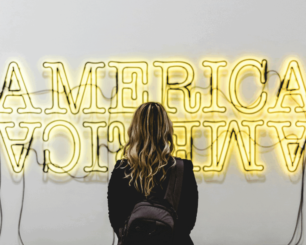 Woman reflectively standing in front of a sign that says "America."